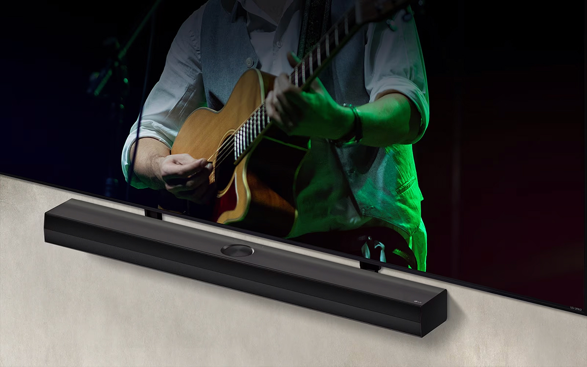 LG Soundbar μπροστά από μαύρο φόντο αποκαλύπτει τη σχεδίασή στην αριστερή γωνία και απομακρύνεται για να δείξει όλο το soundbar. Μια LG QNED TV εμφανίζεται με τον βραχίονα Synergy. Το Soundbar βρίσκεται πάνω στον βραχίονα Synergy, ακουμπά στον τοίχο με την κάτω οθόνη της τηλεόρασης ορατή, δείχνοντας έναν άντρα να παίζει κιθάρα.